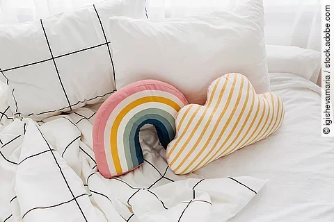 Bett mit weißer Bettwäsche und bunten kleinen Kissen