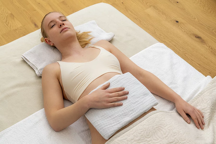 Junge Frau auf einer hellen Decke auf dem Boden liegend mit Dampfauflage.
