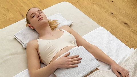 Junge Frau auf einer hellen Decke auf dem Boden liegend mit Dampfauflage.