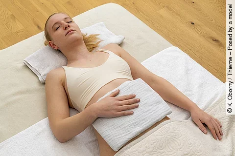 Junge Frau auf einer hellen Decke auf dem Boden liegend mit Dampfauflage.