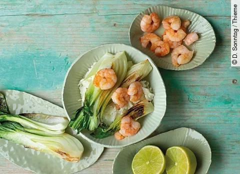 Gesunde Nahrungsmittel auf verschiedenen Tellern: Pak Choi mit Reis und Garnelen, Zitronenhälften, Garnelen, Pak Choi auf türkisem Holzuntergrund
