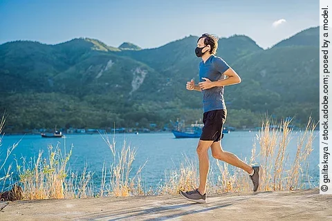 Ein Läufer mit FFP2-Maske joggt an einem Seeufer bei gutem Wetter.