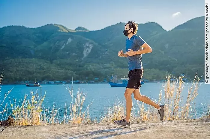 Ein Läufer mit FFP2-Maske joggt an einem Seeufer bei gutem Wetter.