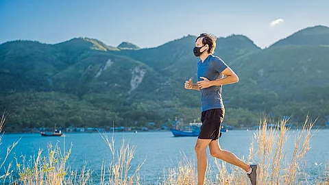 Ein Läufer mit FFP2-Maske joggt an einem Seeufer bei gutem Wetter.