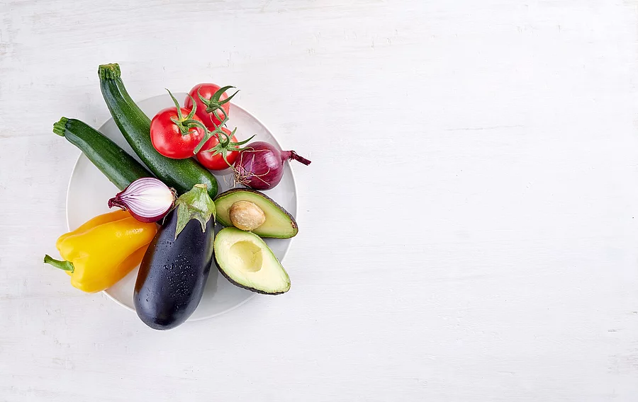 Gemüse: Aubergine, Paprika, Avocado, Zucchini, Tomaten, Zwiebeln auf einem weißen Teller