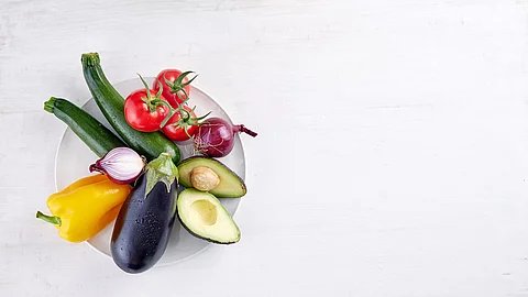 Gemüse: Aubergine, Paprika, Avocado, Zucchini, Tomaten, Zwiebeln auf einem weißen Teller