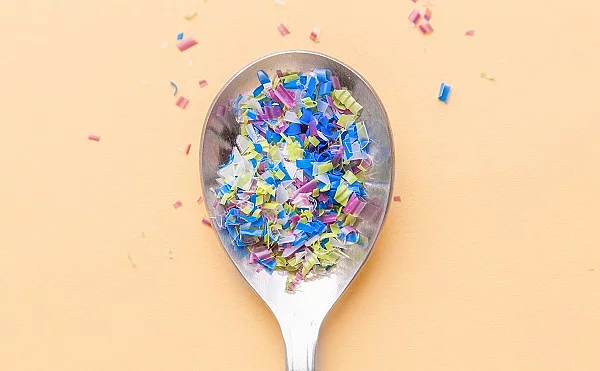 Auf einem Löffel befinden sich kleine bunte Plastikpartikel. Mikroplastik auf Löffel, Umweltverschmutzung