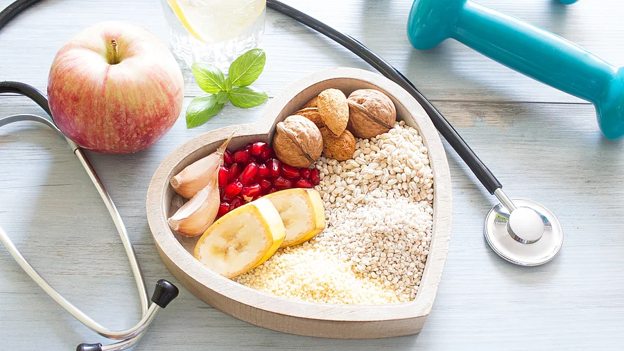 Stethoskop, Hanteln, Apfel, Müsli auf einem Teller in Herzform