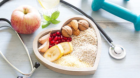 Stethoskop, Hanteln, Apfel, Müsli auf einem Teller in Herzform