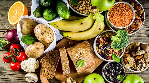 pflanzliche Nahrungsmittel auf Holzuntergrund: Kartoffeln, Bananen, Tomaten, Äpfel, Hülsenfrüchte, Nüsse ...