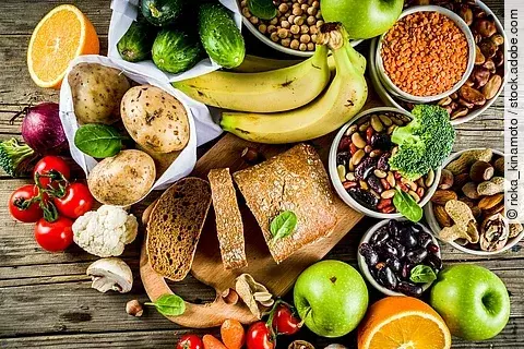 pflanzliche Nahrungsmittel auf Holzuntergrund: Kartoffeln, Bananen, Tomaten, Äpfel, Hülsenfrüchte, Nüsse ...