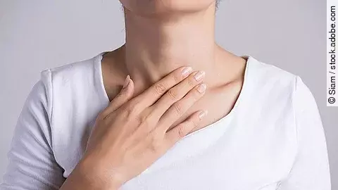 Frau in einem weißen Oberteil fasst sich an den Hals.
