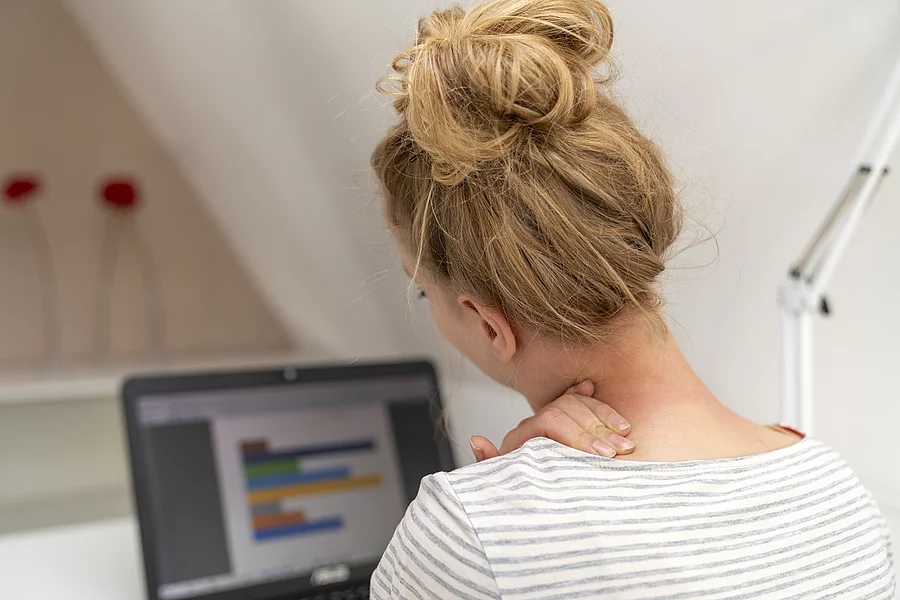 Junge Frau am Schreibtisch hat die Hand am Nacken 