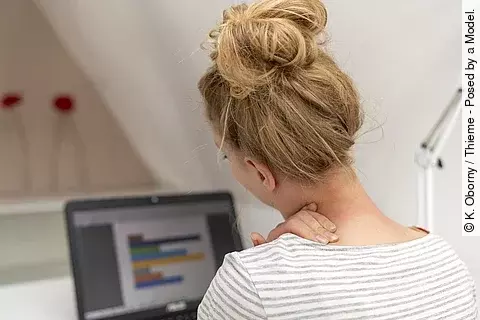 Junge Frau am Schreibtisch hat die Hand am Nacken 