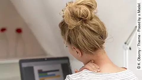 Junge Frau am Schreibtisch hat die Hand am Nacken 