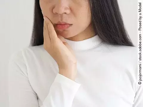 Frau mit asiatischem Aussehen fasst sich an den Kiefer.