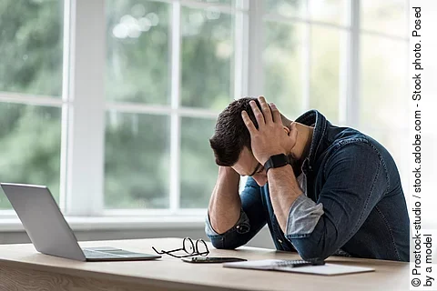 Mann sitzt gestresst am Schreibtisch und schlägt die Hände über dem Kopf zusammen