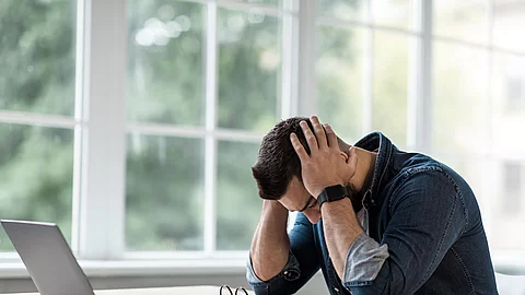 Mann sitzt gestresst am Schreibtisch und schlägt die Hände über dem Kopf zusammen