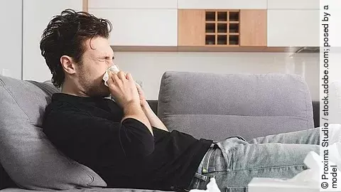 Mann mit Schnupfen liegt auf dem Sofa und putzt sich die Nase