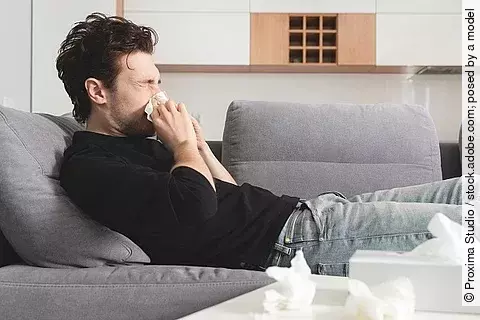 Mann mit Schnupfen liegt auf dem Sofa und putzt sich die Nase