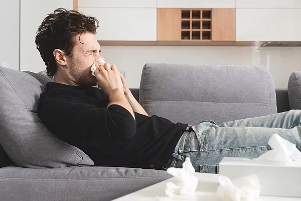 Mann mit Schnupfen liegt auf dem Sofa und putzt sich die Nase