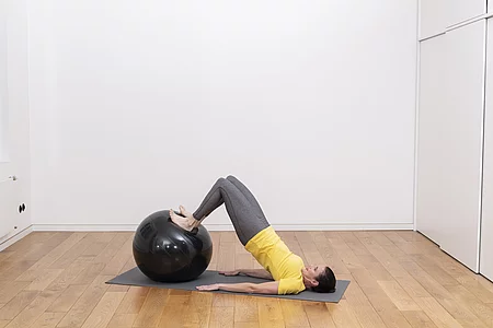 Frau trainiert mit Gymnastikball die Übung Zugbrücke.