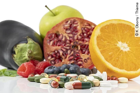 Frische Früchte, Tabletten und Kapseln vor weißem Hintergrund.