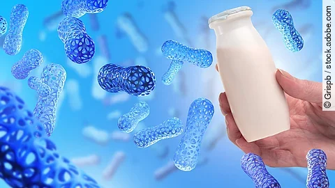 Illustration: blau eingefärbte Bakterien in blauem Umfeld, eine Hand hält ein Fläschchen mit Joghurt