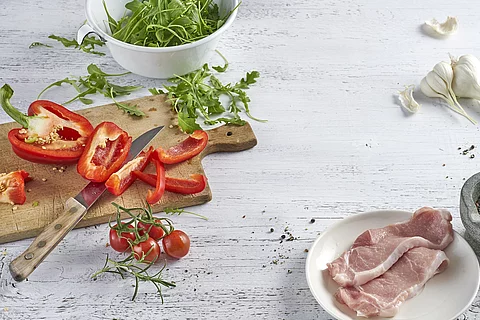 rohes Steak, Paprika, Rucola und Knoblauch auf weißem Holztisch