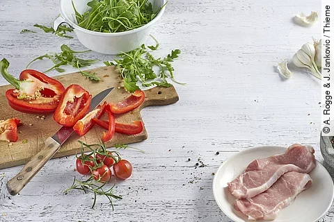rohes Steak, Paprika, Rucola und Knoblauch auf weißem Holztisch