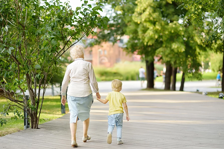 Beautiful granny and her little grandchild walking together in park. Oma mit Enkel an der Hand beim Parkspaziergang