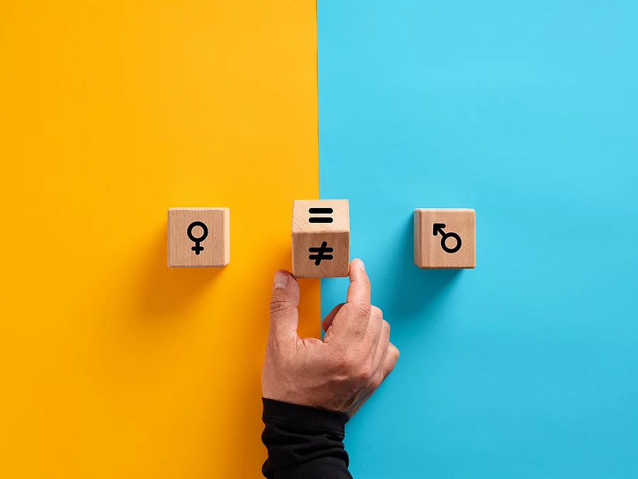 2 Holzwürfel, links mit weiblichem, rechts mit männlichem Symbol; in der Mitte dreht eine Hand einen Würfel mit dem Ungleich-Symbol