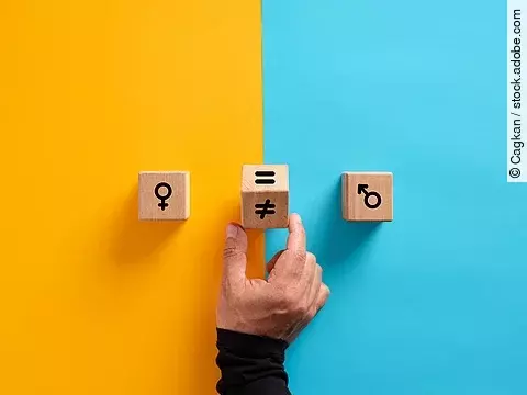 2 Holzwürfel, links mit weiblichem, rechts mit männlichem Symbol; in der Mitte dreht eine Hand einen Würfel mit dem Ungleich-Symbol
