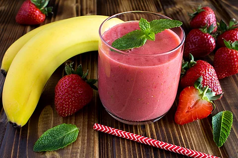 Smoothie aus Banane und Erdbeeren, hübsch arrangiert mit frischen Früchten und Pfefferminzblättern auf einem Holztisch