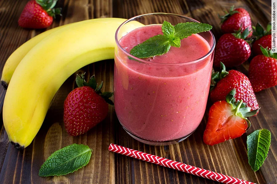 Smoothie aus Banane und Erdbeeren, hübsch arrangiert mit frischen Früchten und Pfefferminzblättern auf einem Holztisch