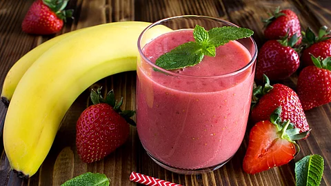 Smoothie aus Banane und Erdbeeren, hübsch arrangiert mit frischen Früchten und Pfefferminzblättern auf einem Holztisch