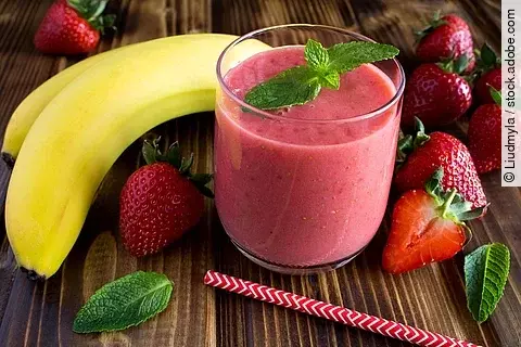 Smoothie aus Banane und Erdbeeren, hübsch arrangiert mit frischen Früchten und Pfefferminzblättern auf einem Holztisch