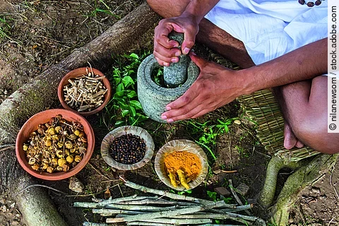 Mann mörsert Gewürze auf dem Boden sitzend.