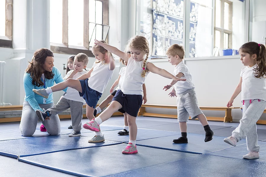Just a little higher! Kinder und Lehrerin in einer Turnhalle