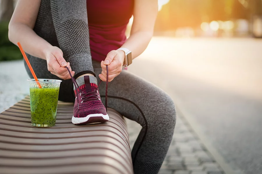 Green detox smoothie cup and woman lacing shoes before workout. Grüner Detox Smoothie und eine Frau in Sportschuhen