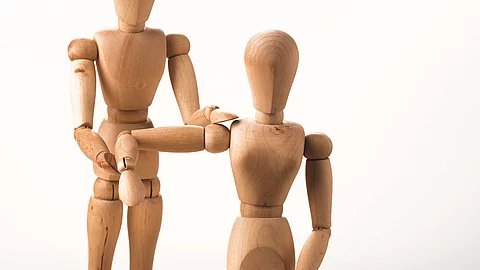 2 Holzmännchen: Das eine behandelt die Schulter des anderen