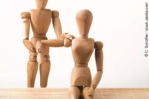 2 Holzmännchen: Das eine behandelt die Schulter des anderen