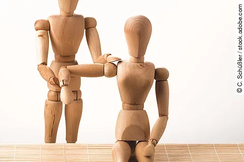 2 Holzmännchen: Das eine behandelt die Schulter des anderen
