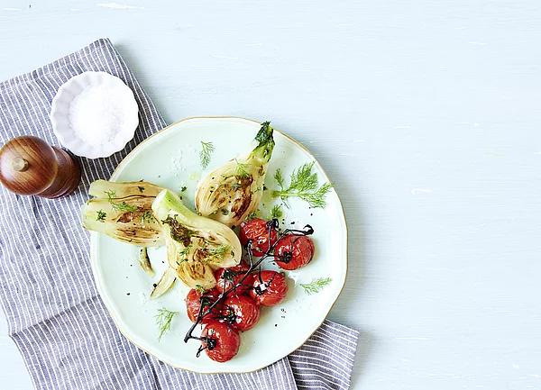 Fenchel-Tomaten-Gemüse auf weißem Teller und gestreiftem Tuch in Szene gesetzthtet