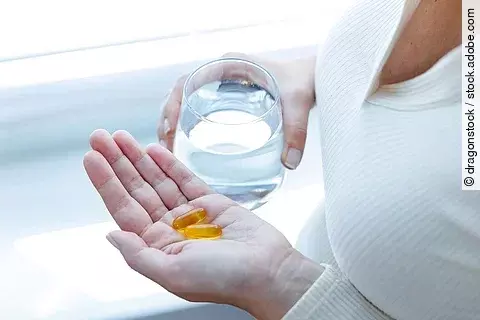Frau hält Nahrungsergänzungsmittel in der Hand und in der andern ein Glas  mit Wasser.