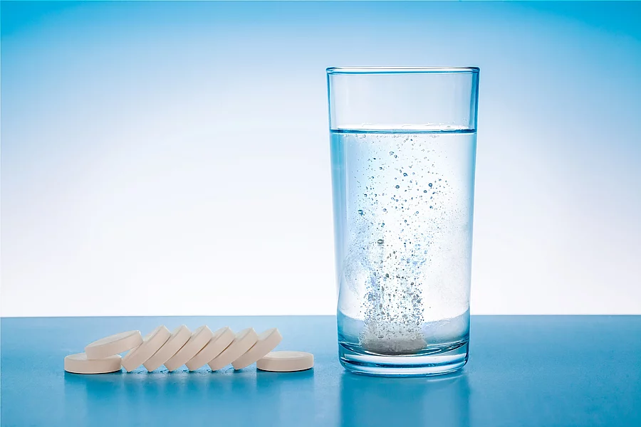 Wasserglas mit sprudelnder Tablette, daneben Tabletten