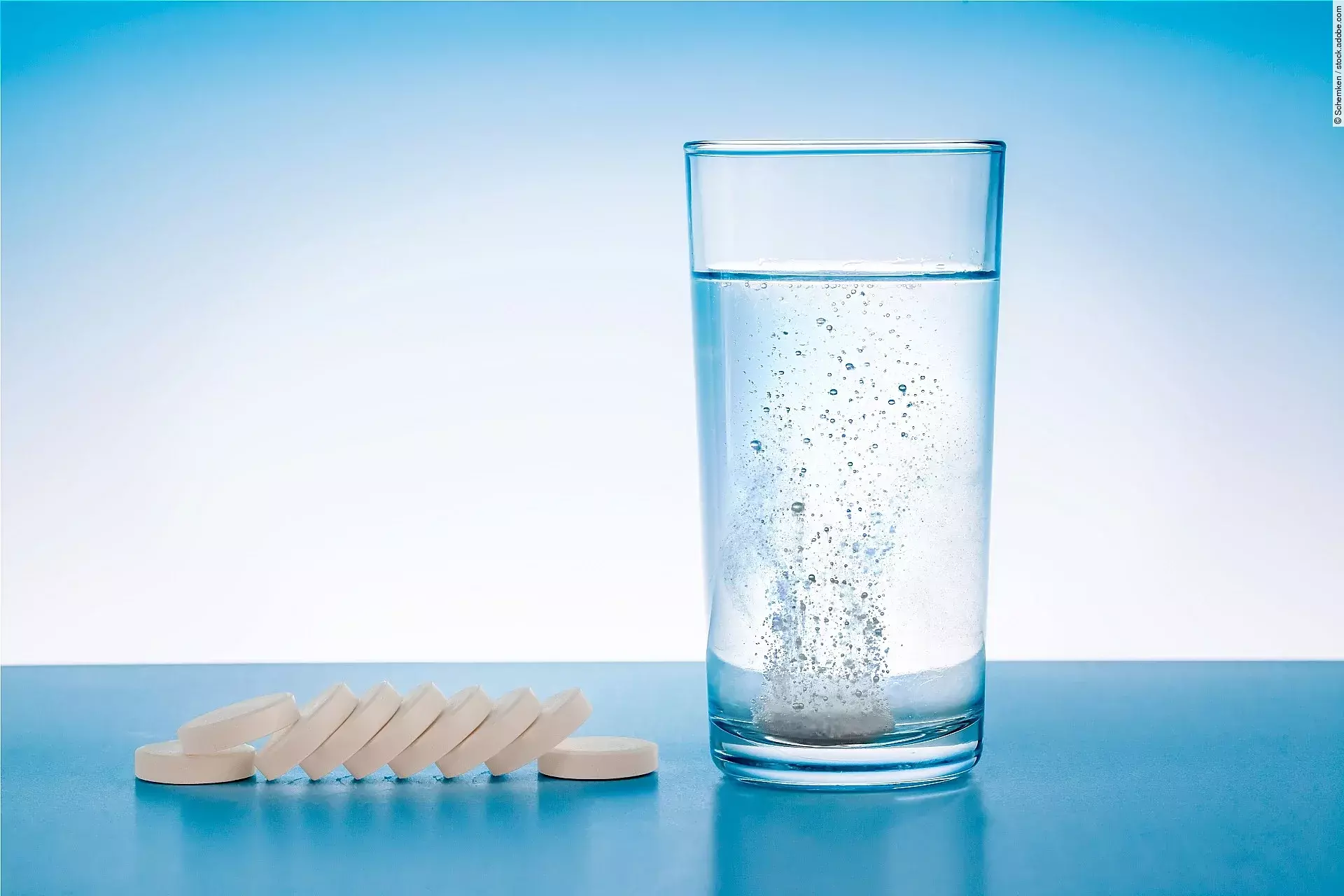 Wasserglas mit sprudelnder Tablette, daneben Tabletten