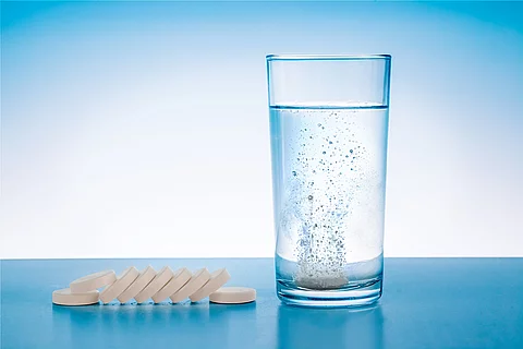 Wasserglas mit sprudelnder Tablette, daneben Tabletten