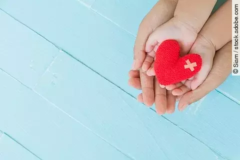 Erwachsener hält Kinderhände, die ein Stoffherz halten.