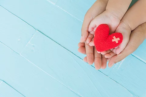Erwachsener hält Kinderhände, die ein Stoffherz halten.